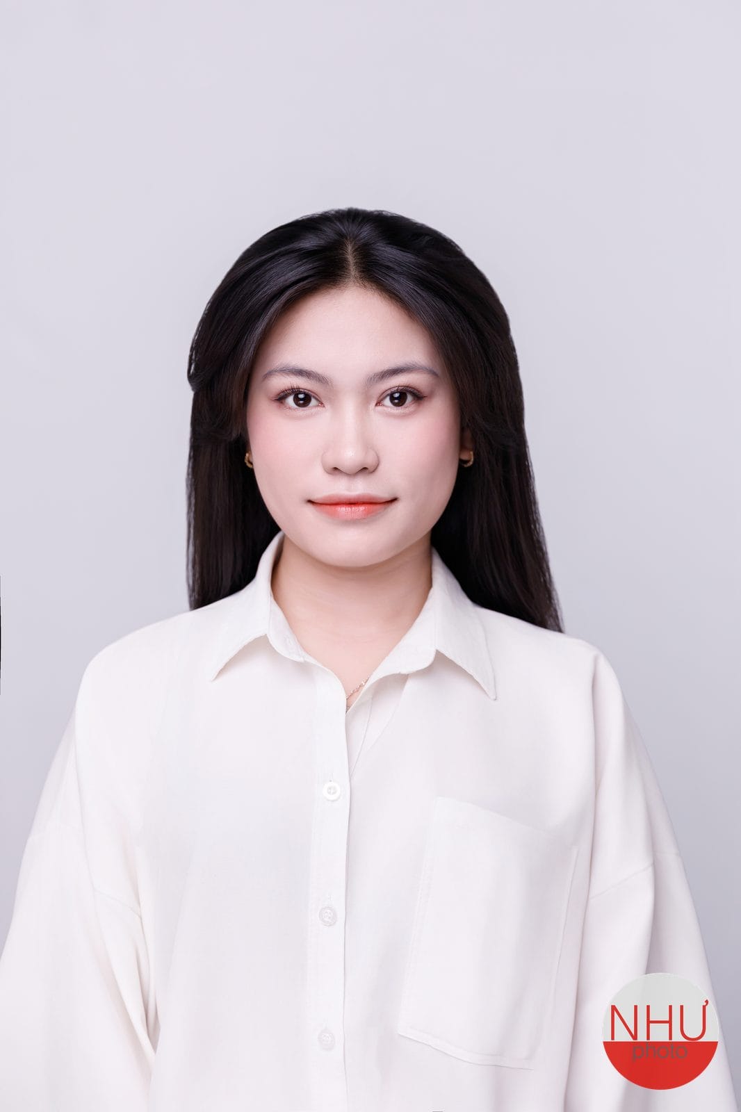 Ảnh thẻ nền xám nhạt: cô gái tóc đen dài thẳng mặc sơ mi trắng ngà có túi ngực, mỉm cười nhẹ, góc dưới có logo NHƯ photo