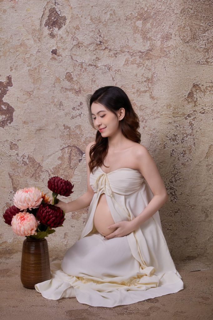 Mẹ bầu ngồi bên bình hoa tươi trước phông tường đá, chụp ảnh bầu tại NHƯ Photo