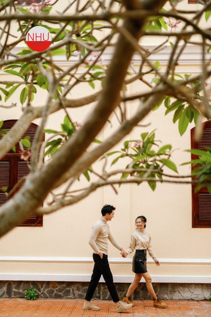 Cặp đôi nắm tay dạo bước trước nhà cổ tường vàng, ảnh cưới ngoại cảnh